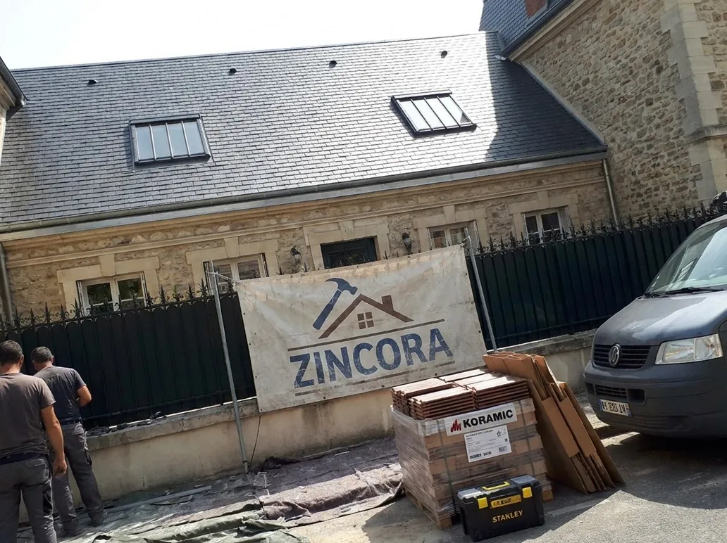 Toiture en ardoise refaite par Zincora sur une maison en pierre de Saint-Germain-en-Laye, avec fenêtres de toit et bâche de l’entreprise sur la grille